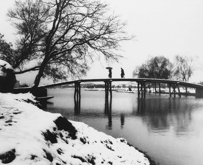 Two people crossing a snow-covered bridge